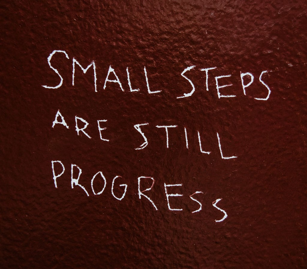 Words scratched on a wall, "small steps are still progress"